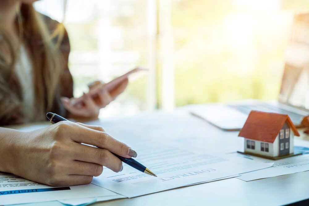 Woman Signing Documents at a Desk With a Toy House, Holding a Phone — Hannaway Lawyers in Port Macquarie, NSW
