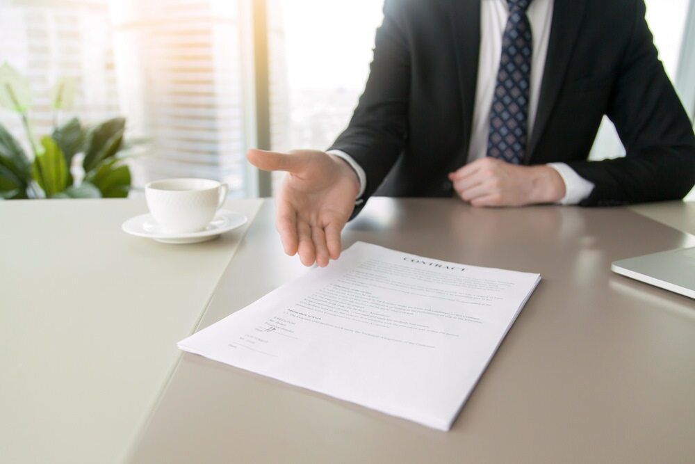 Man in Suit Reaching Towards a Contract on a Desk, Inviting a Handshake — Hannaway Lawyers in Port Macquarie, NSW