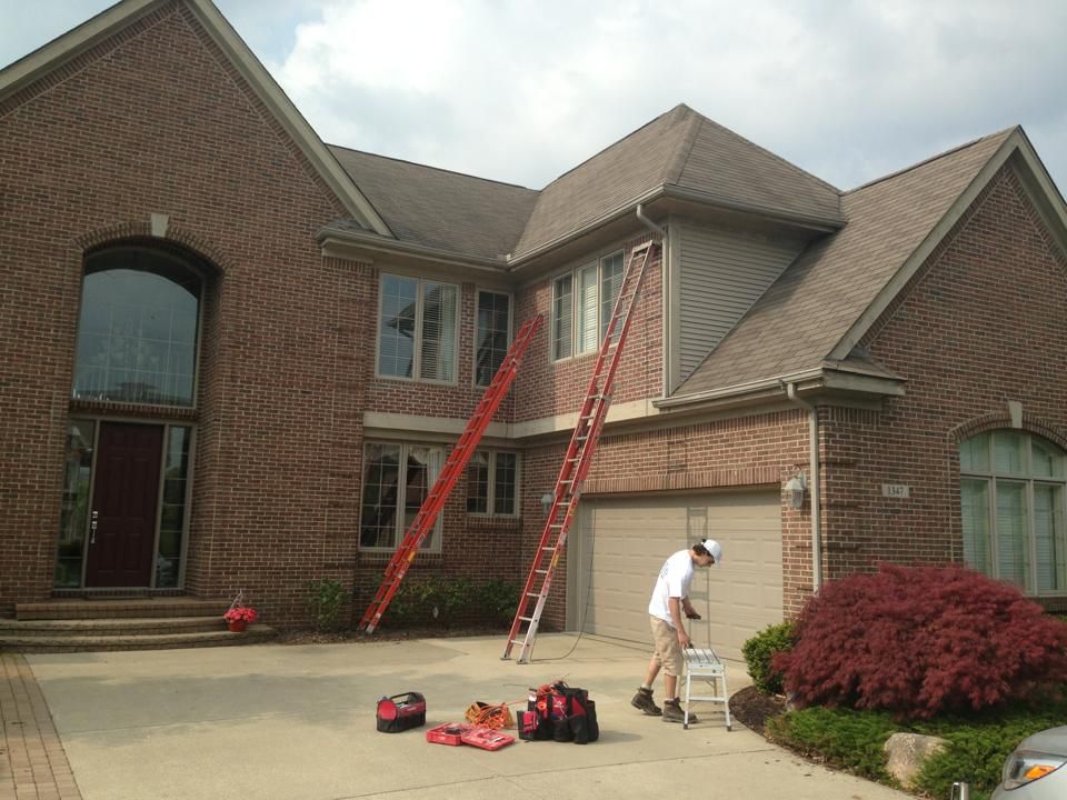 A man with a ladder standing in front of a large brick house