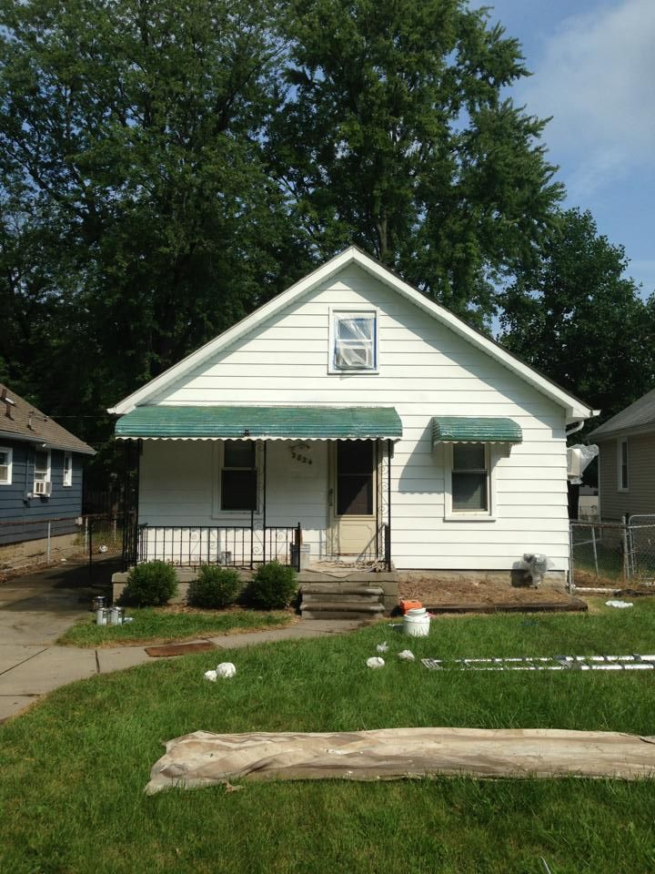 A small white house with a green awning on the porch
