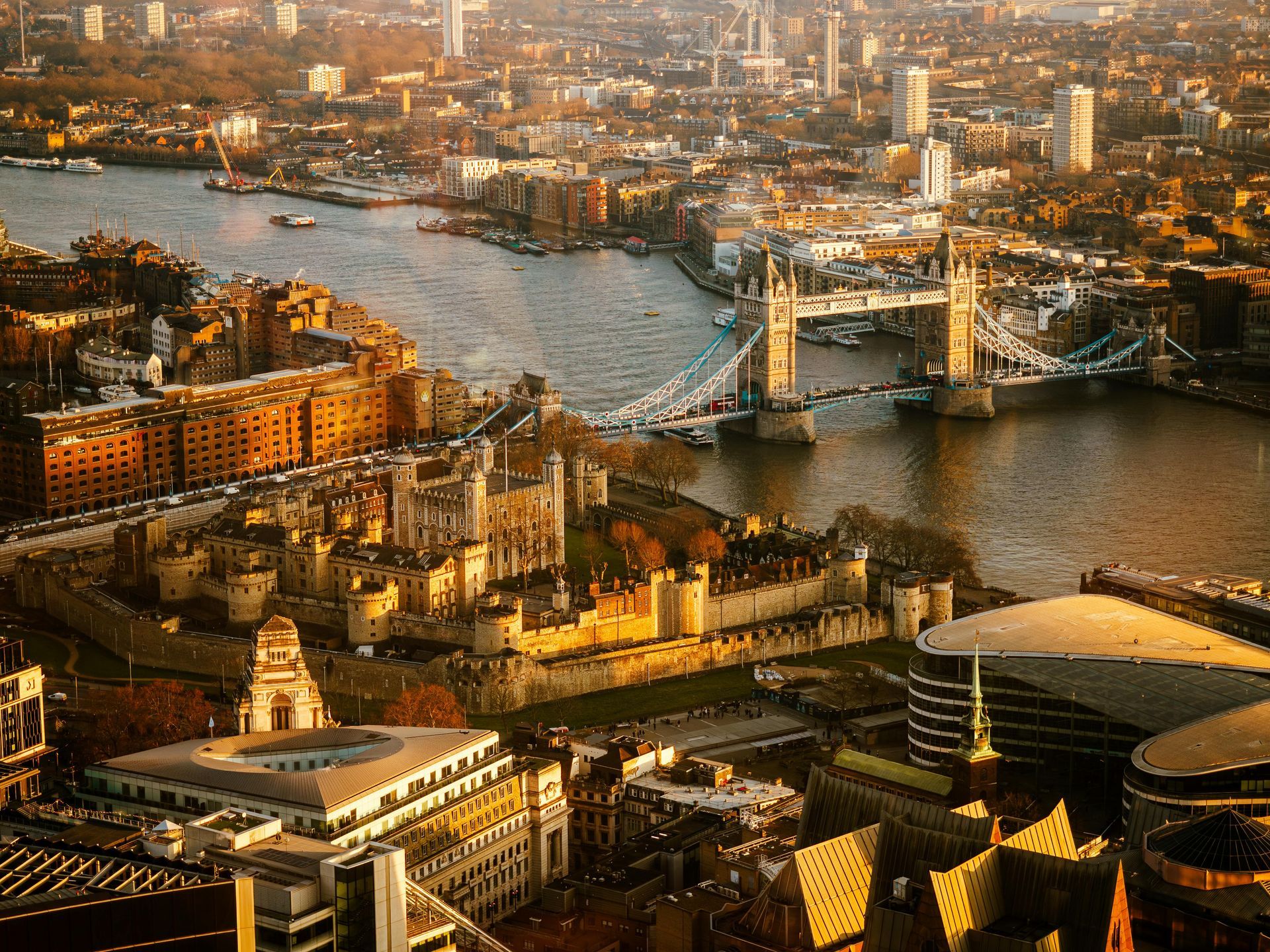Aerial view of the Tower of London and Tower Bridge spanning the River Thames in London at golden hour.