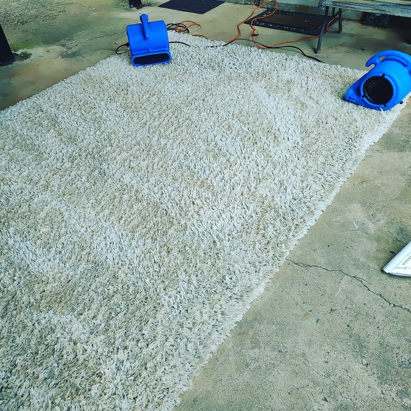 A white rug is sitting on a concrete floor next to a blue fan.