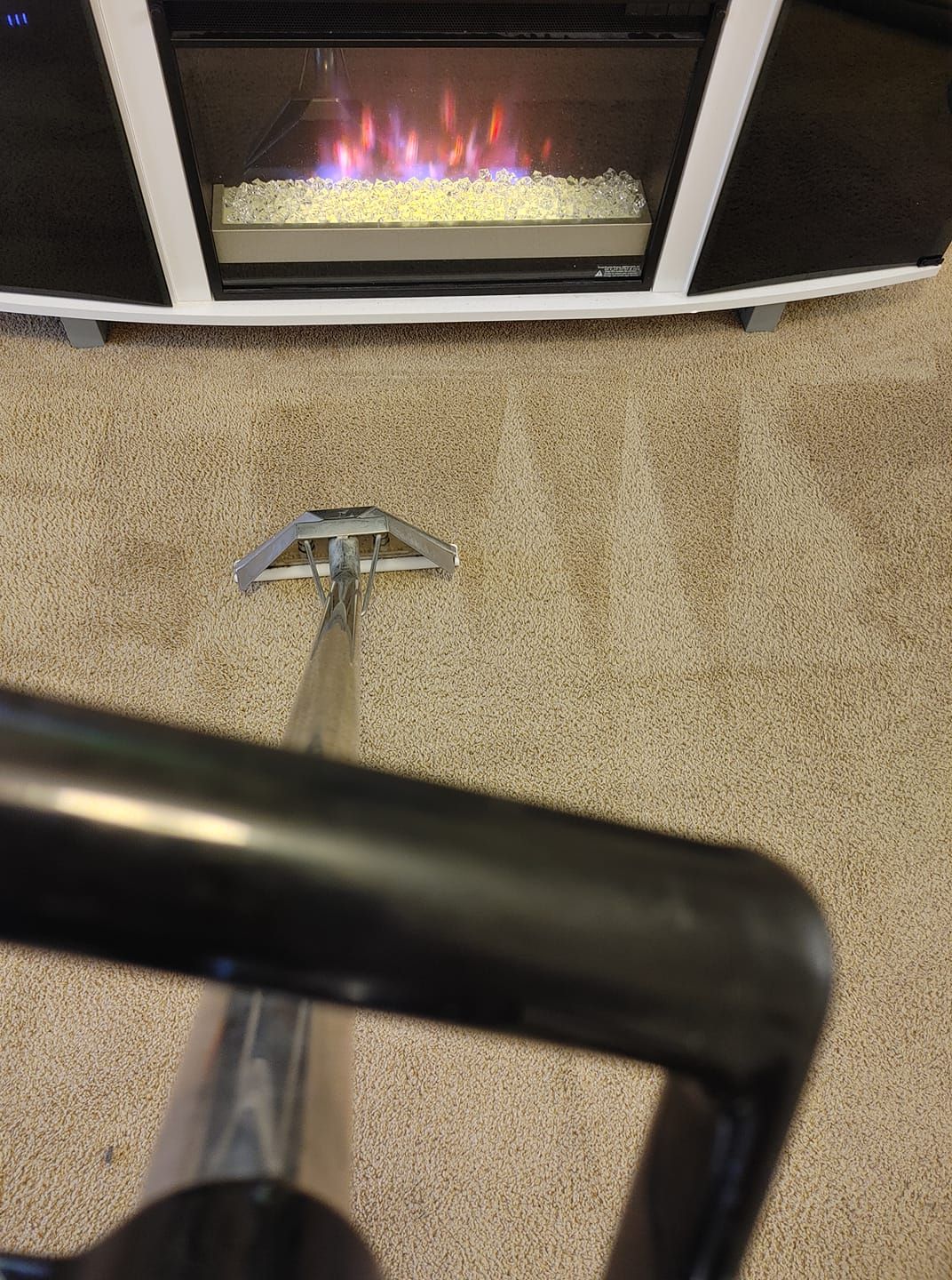 A vacuum cleaner is cleaning a carpet next to a fireplace.