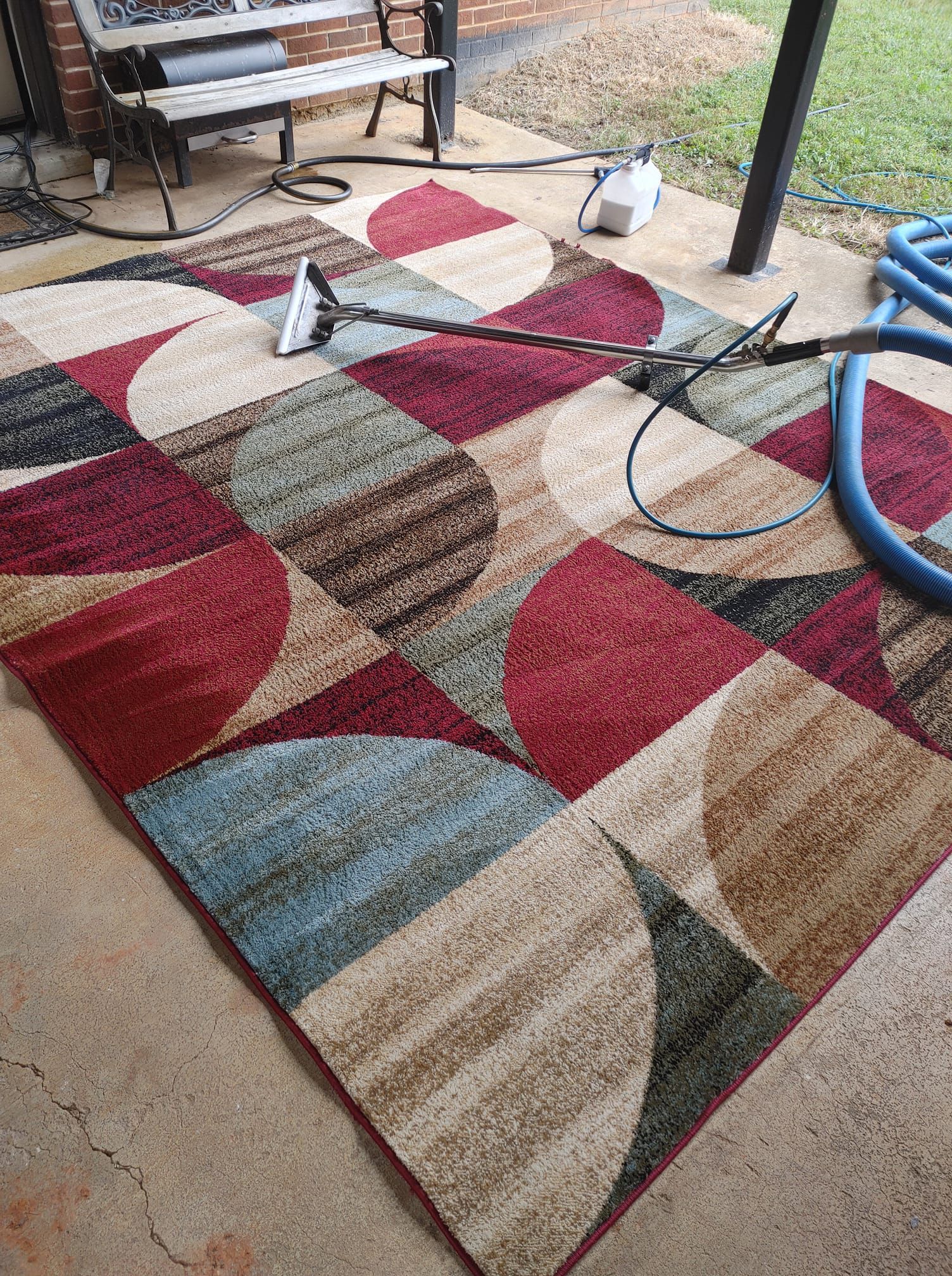 A rug is being cleaned with a vacuum cleaner on a patio.