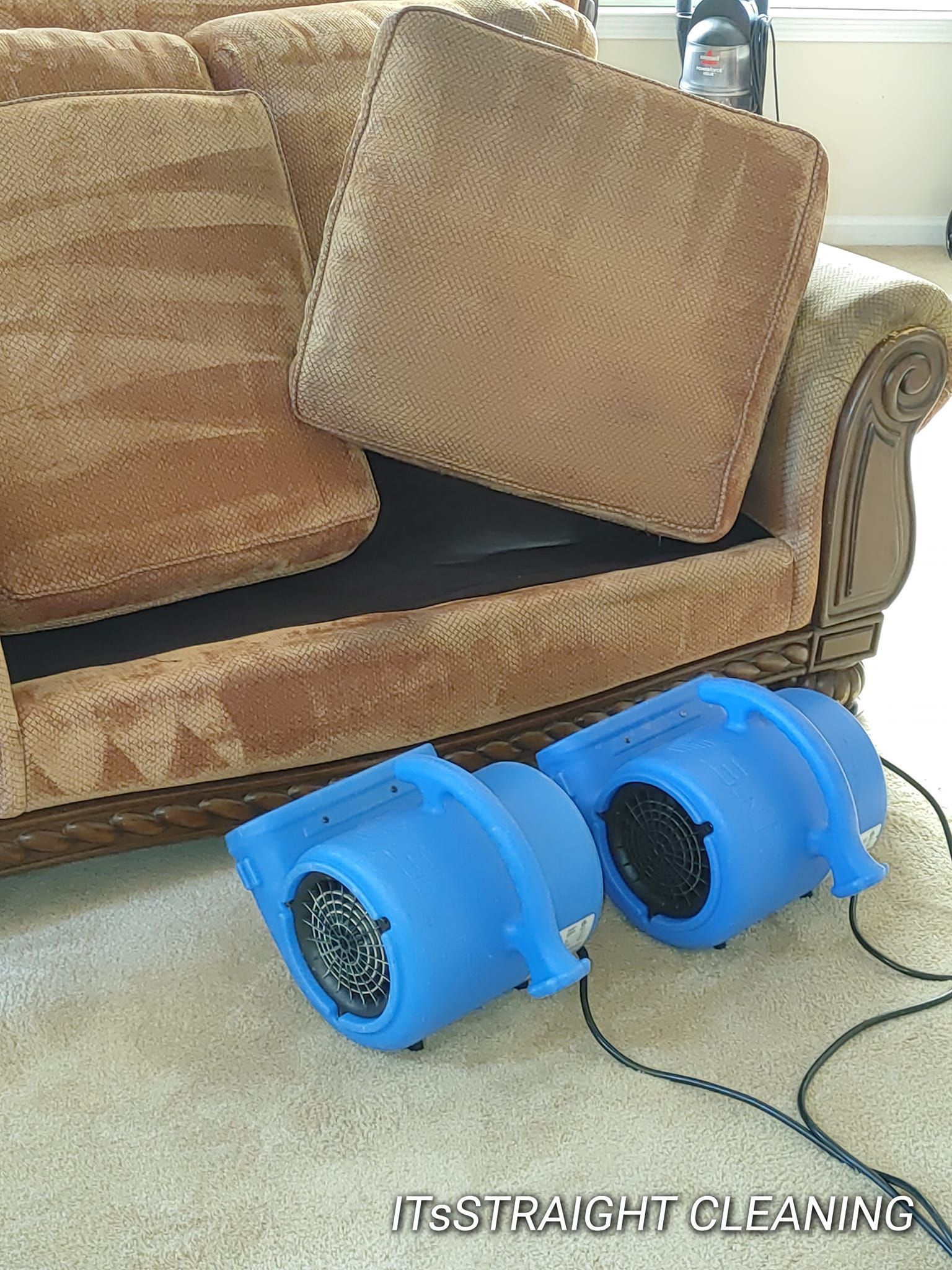 Two blue fans are sitting next to a couch in a living room.