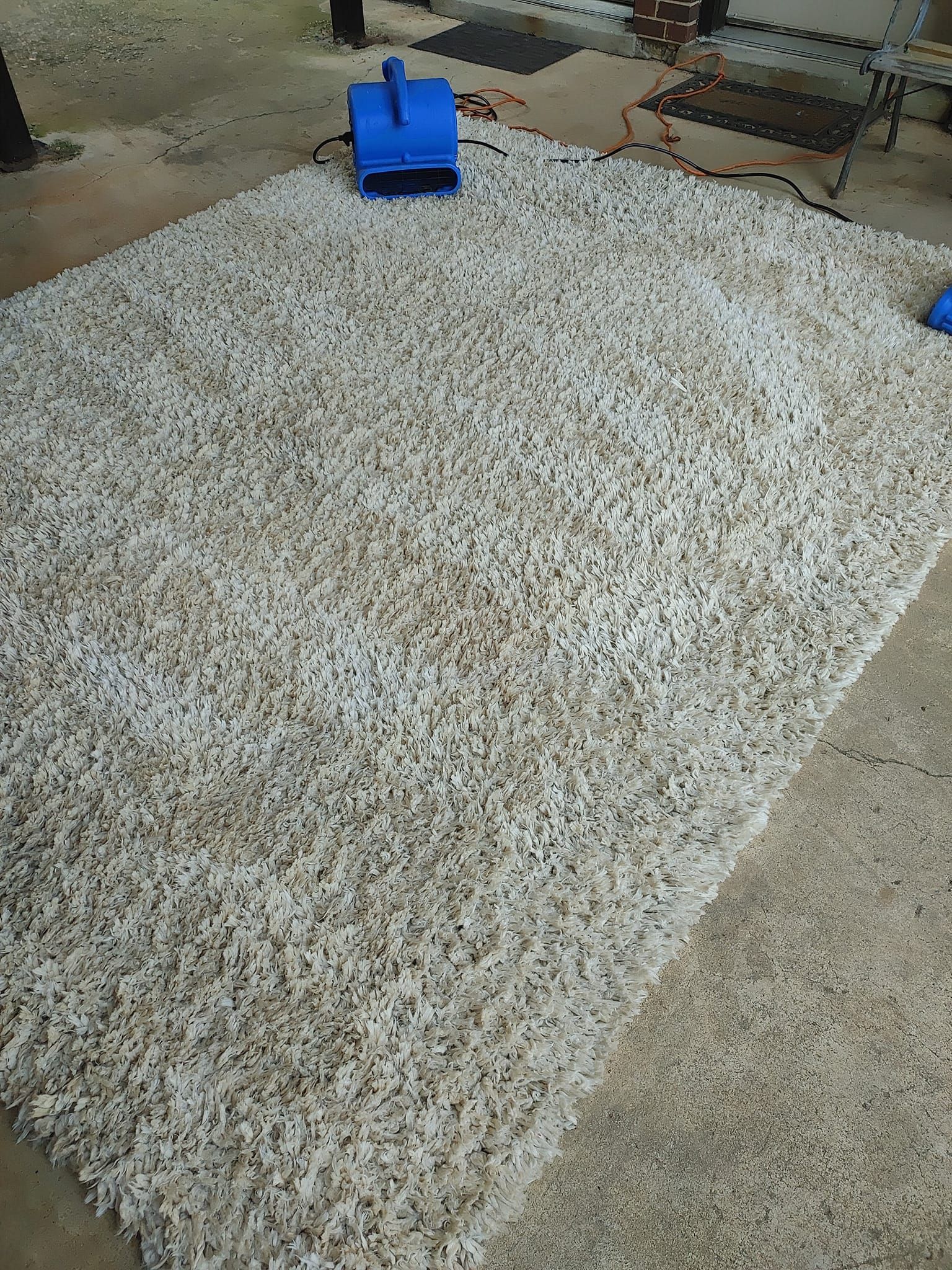 A large white rug is sitting on the ground next to a blue fan.