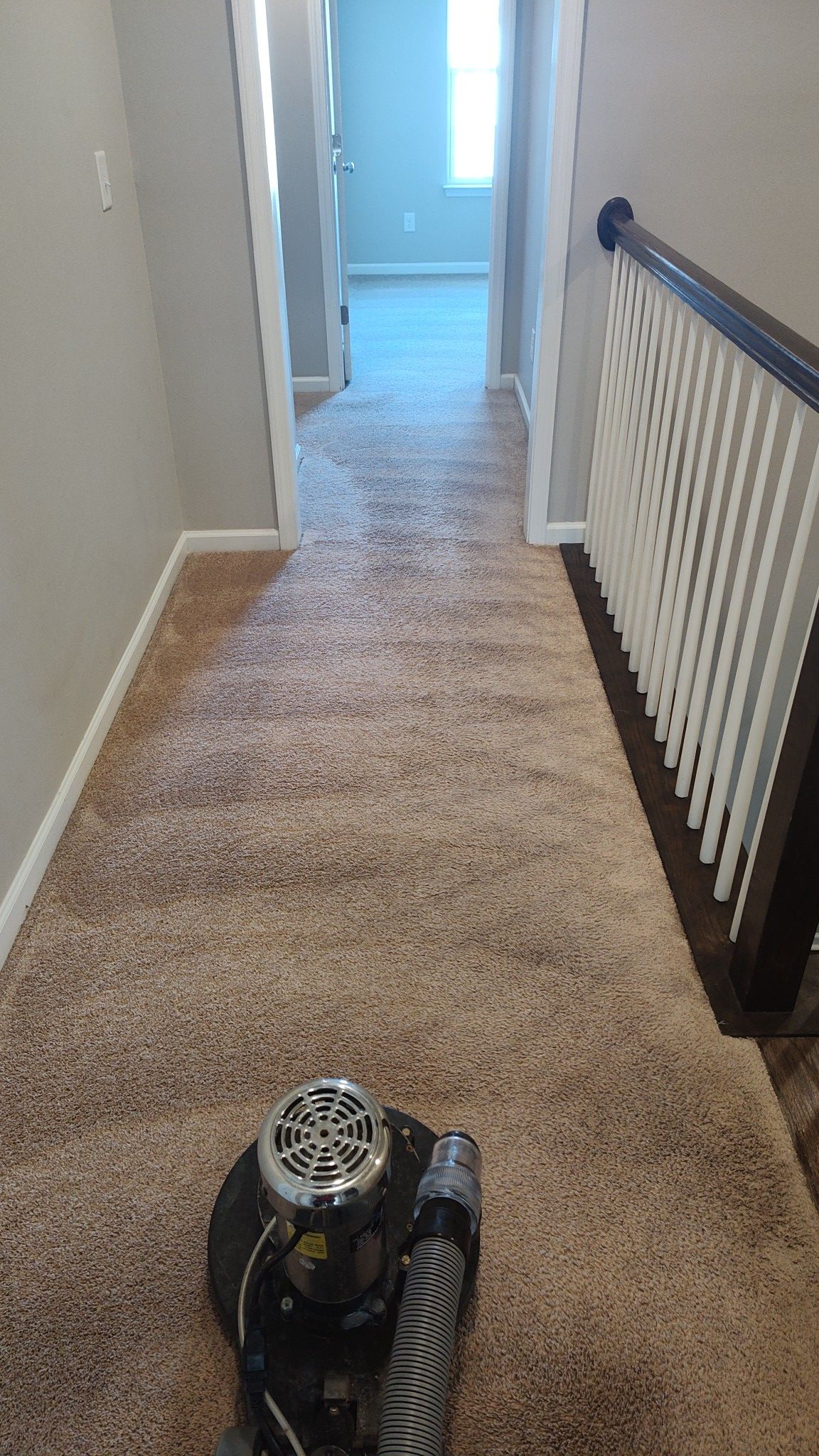 A vacuum cleaner is sitting on a carpeted hallway next to a staircase.