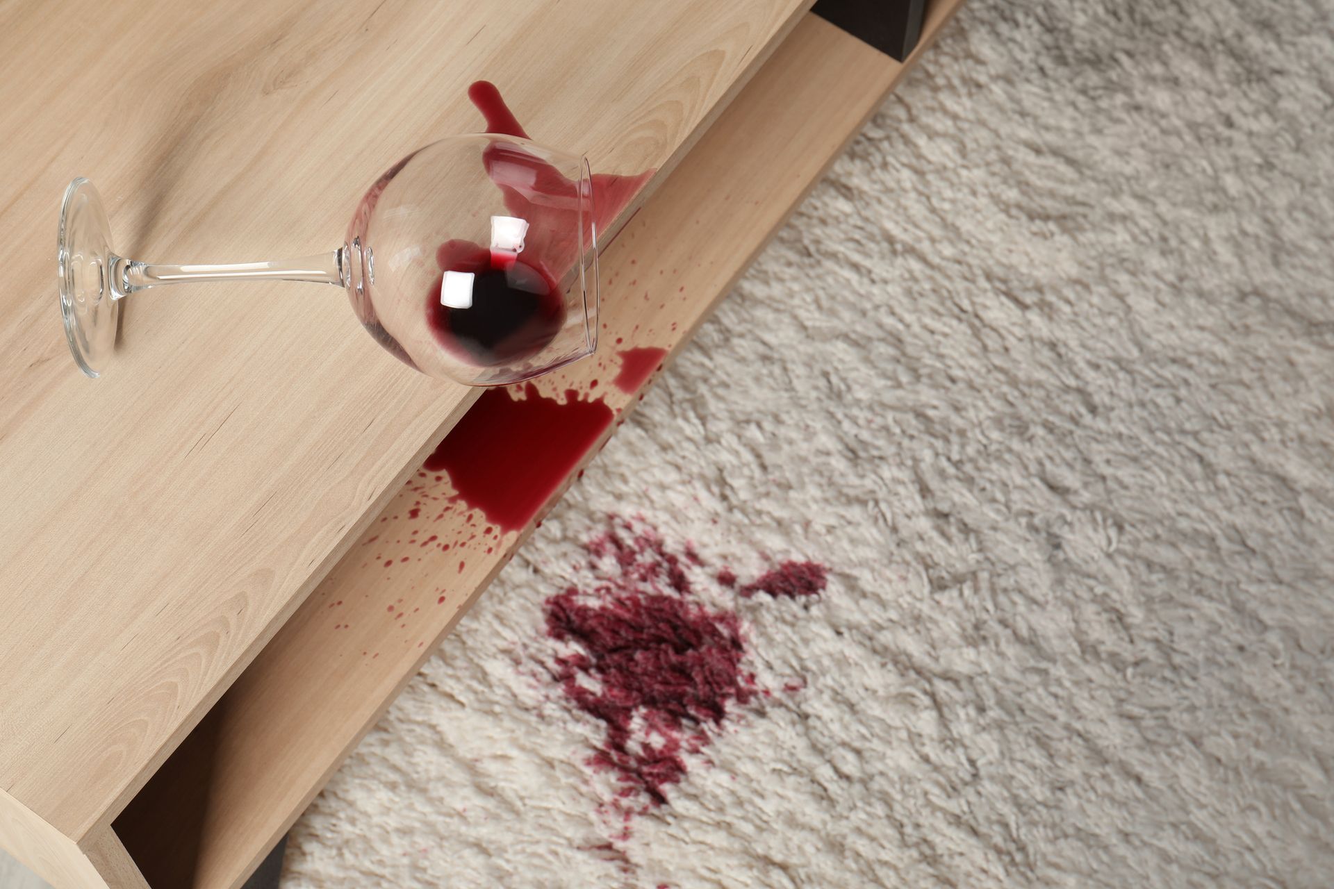 A glass of red wine spilled on a carpet.