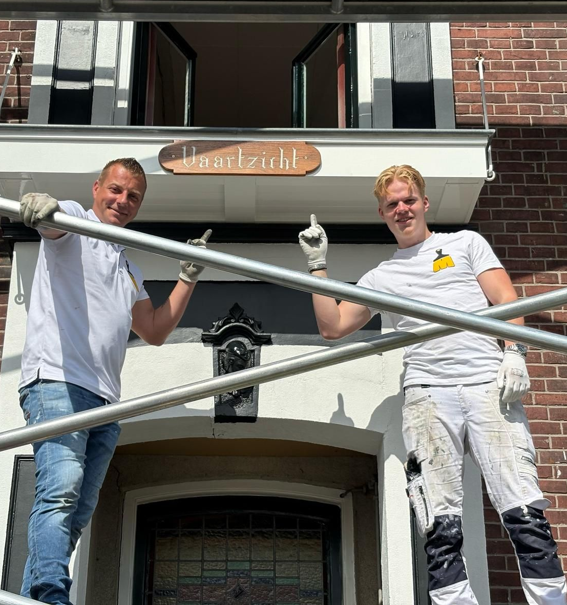 Twee mannen op een steiger wijzen naar de ingang van een huis, met daarboven het bord 'Havelzicht'.