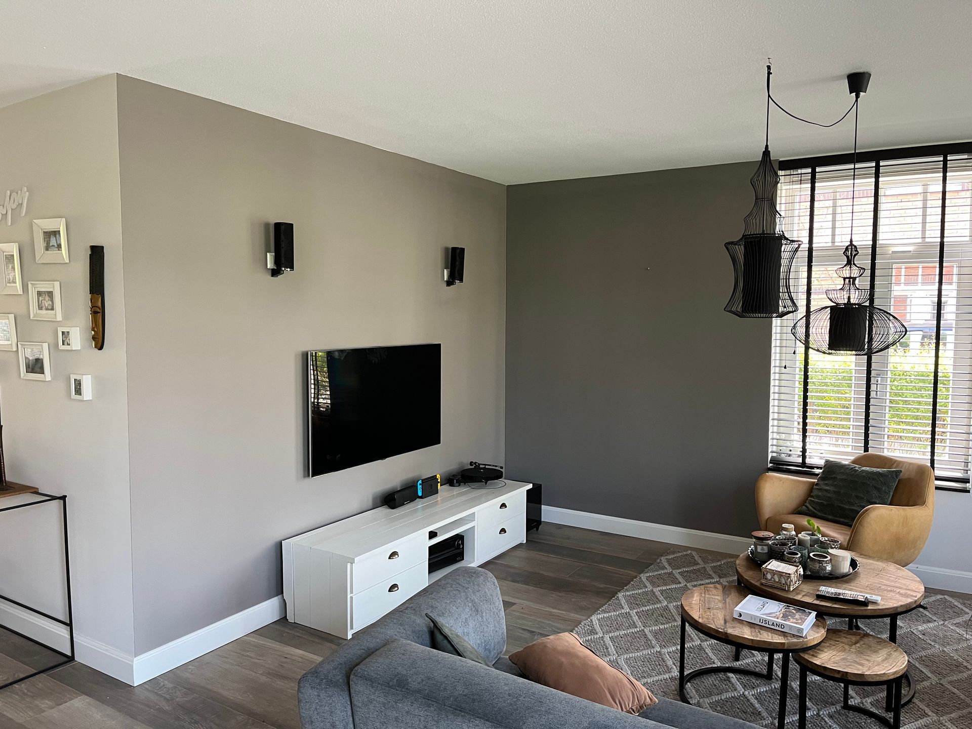 Woonkamer met grijze muren, tv, luidsprekers en modern meubilair.