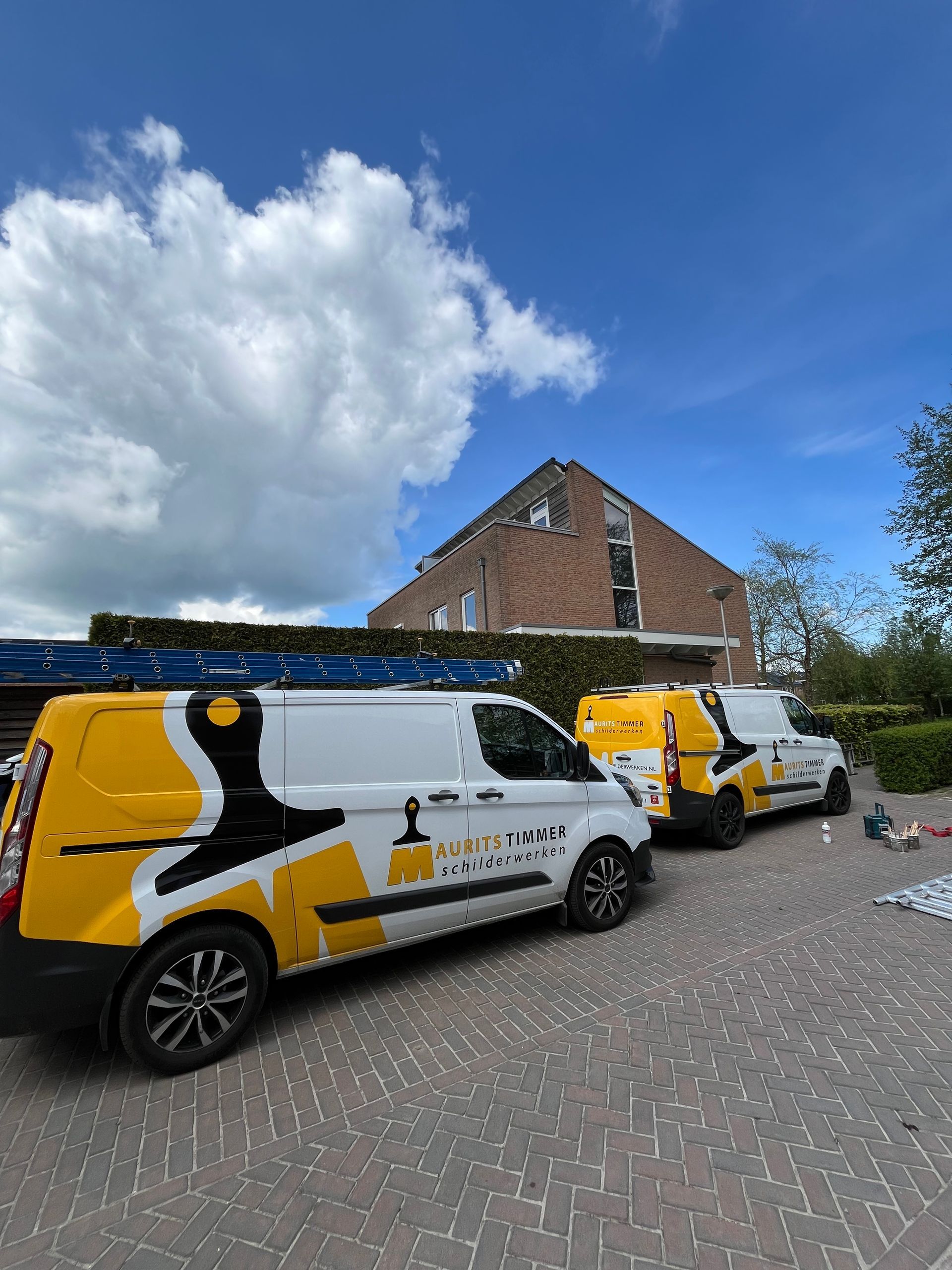 Drie witte busjes met geel-zwarte logo's geparkeerd voor een huis op een zonnige dag.