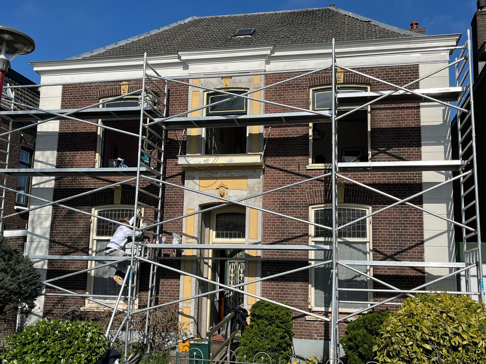 Renovatie van een gevel met steigers. Een arbeider op een steiger, met bakstenen en gele afwerking.