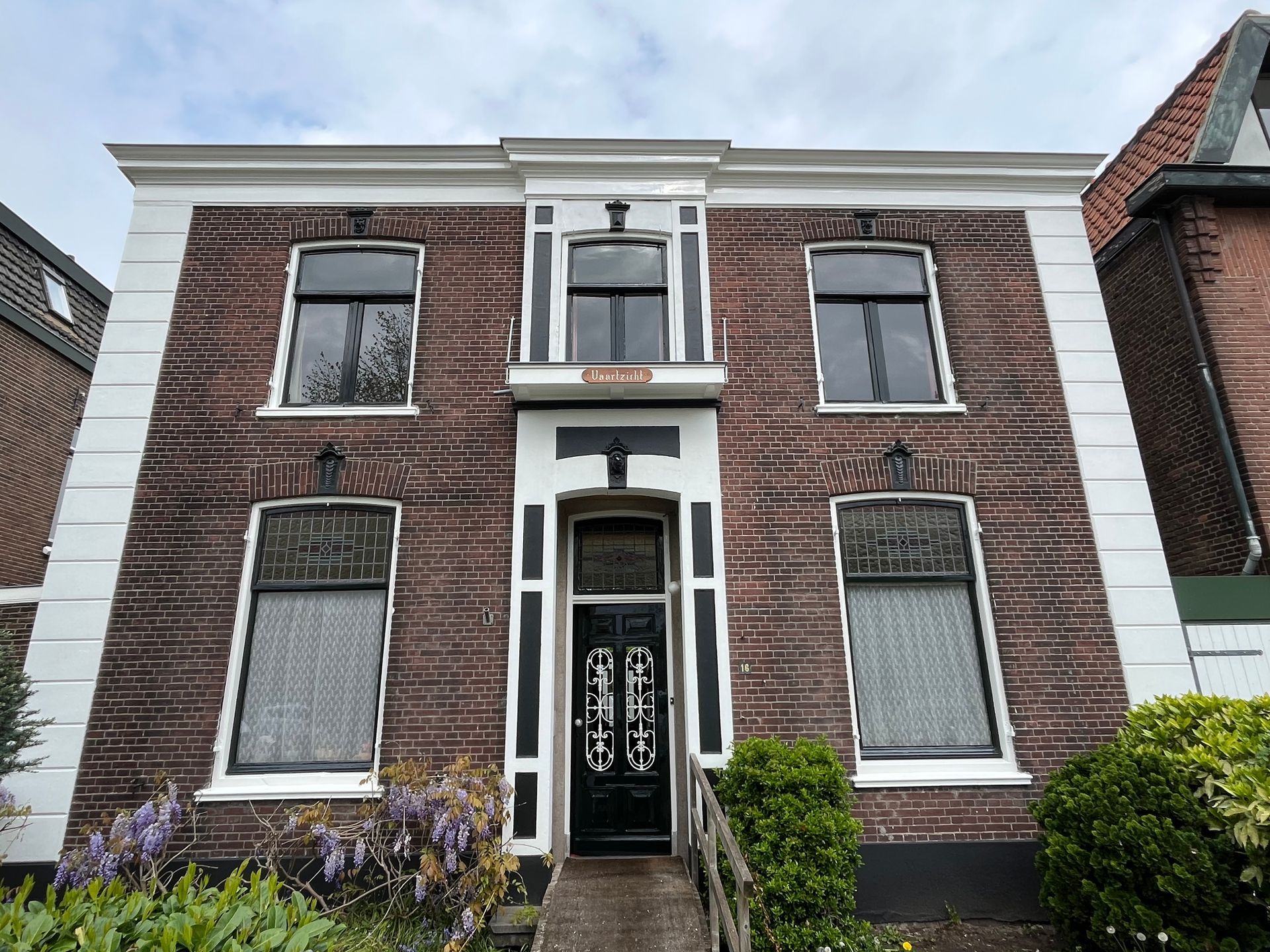 Bakstenen huis met zwarte ramen en deur, witte kozijnen en een kleine veranda.