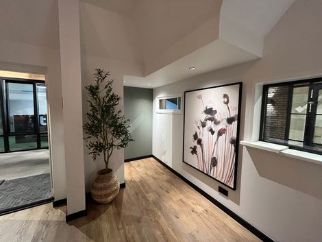 Hal met houten vloer, plant in rieten mand, bloemenkunstwerk en een raam.