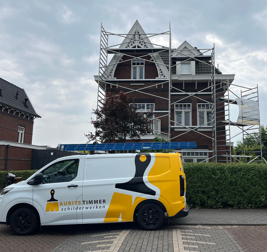 Witte bestelwagen met logo geparkeerd voor een huis dat gerenoveerd wordt, steigers aanwezig.