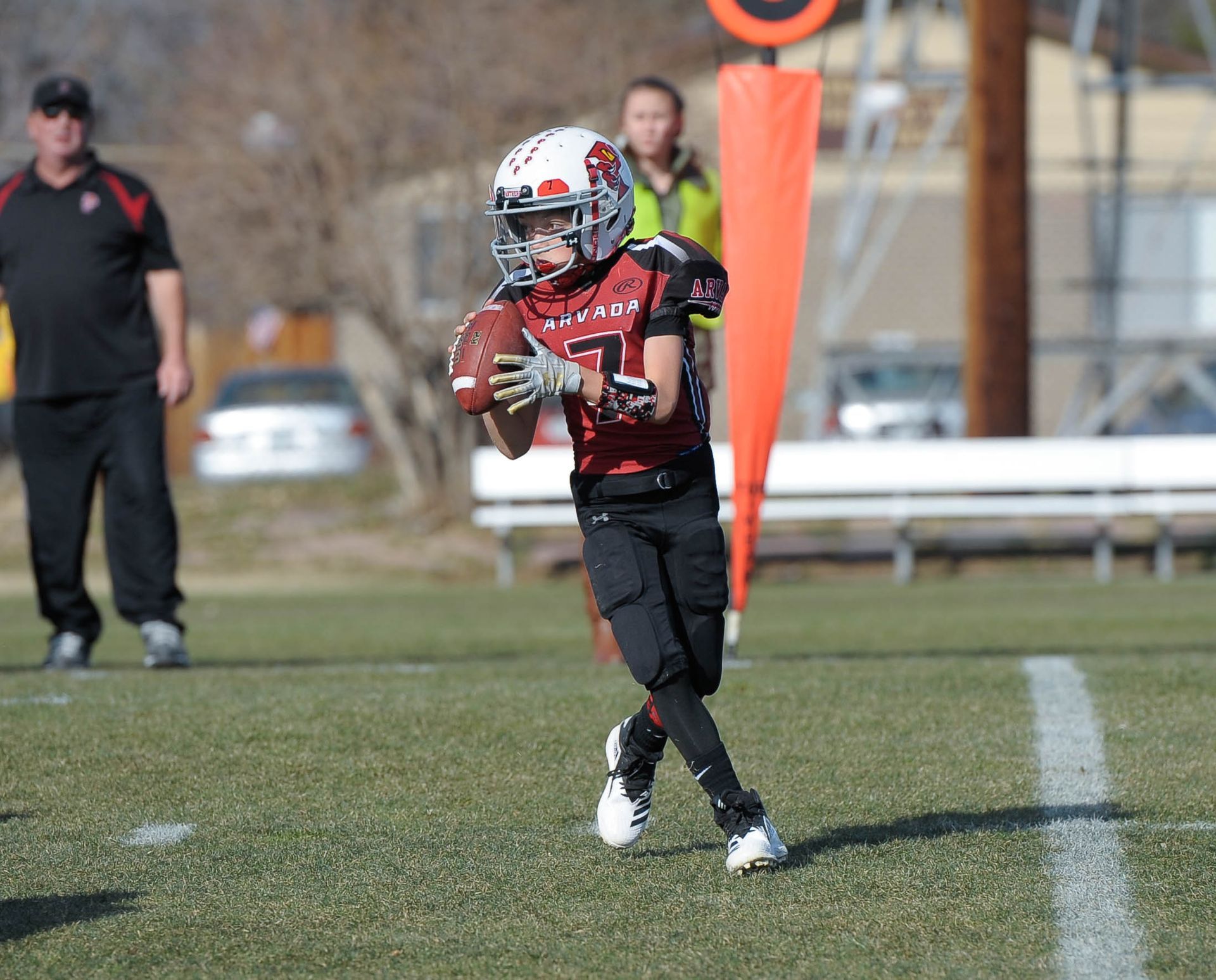 Flag football game at night, a player in red jersey runs with the ball as others pursue on a green field.