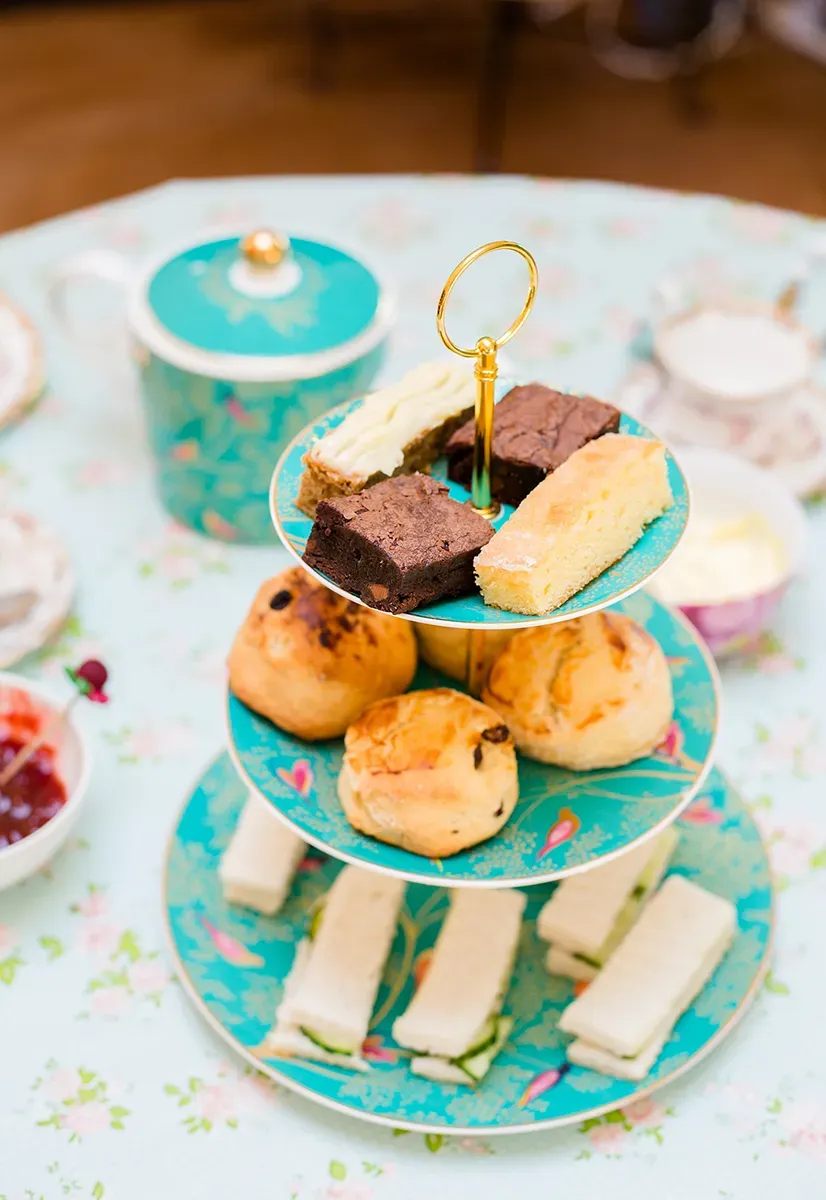 A three tiered tray filled with pastries and sandwiches on a table.