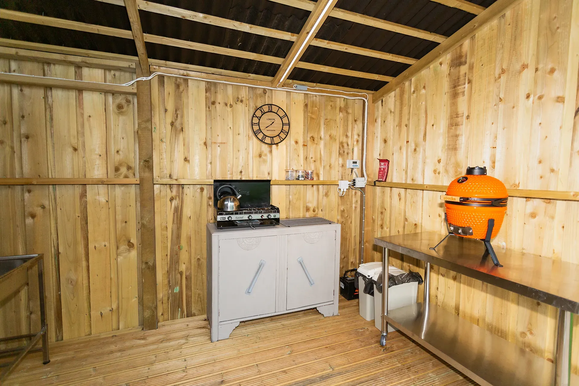 A wooden shed with a stove and a table in it.