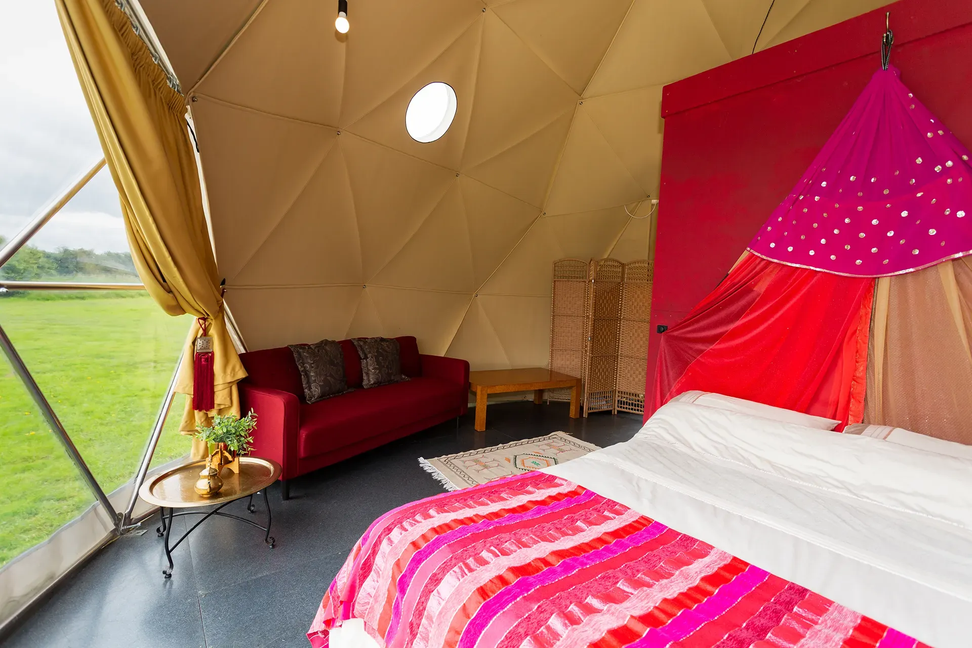 A bedroom in a dome tent with a bed , couch and table.