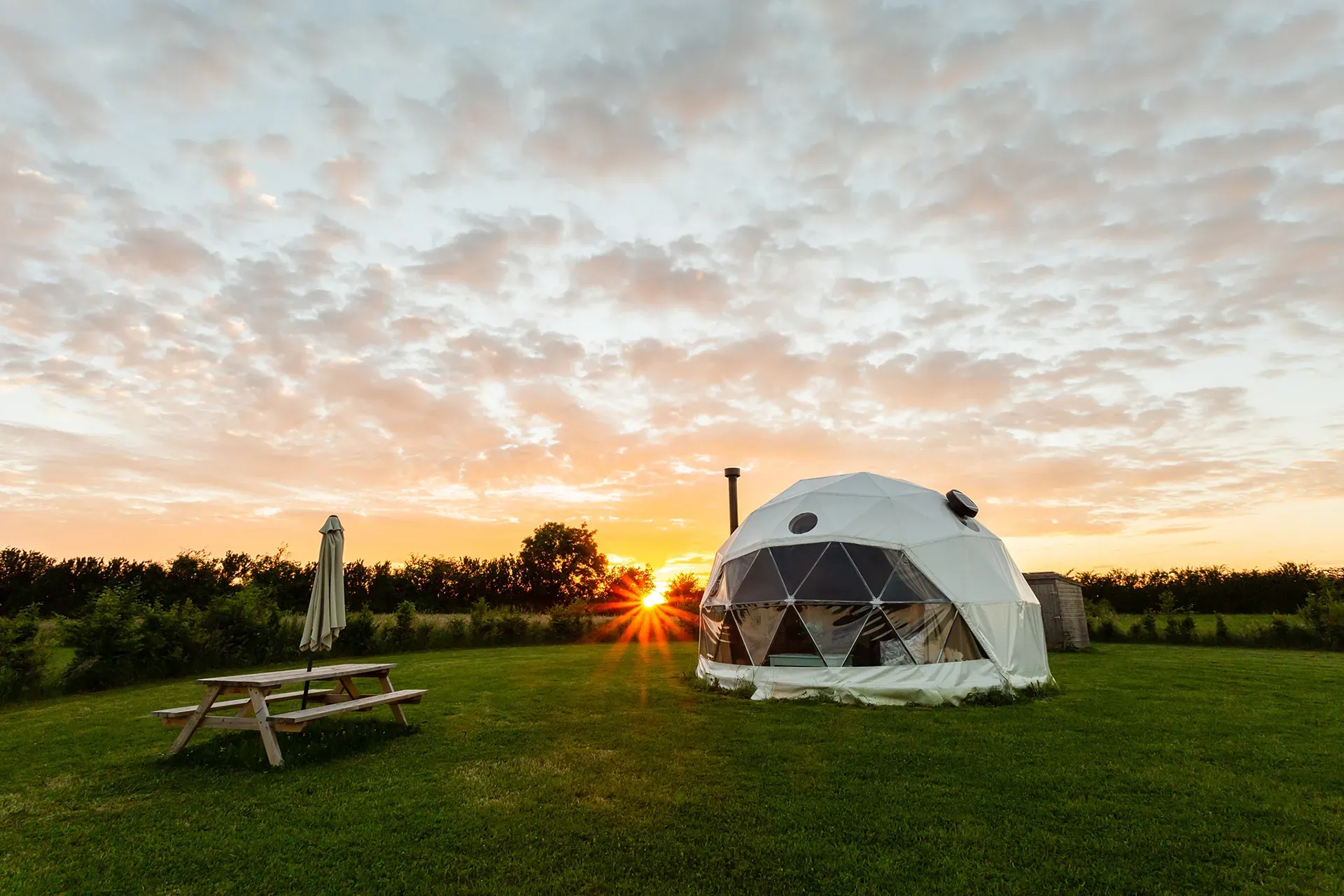 A dome tent is sitting in the middle of a grassy field at sunset.