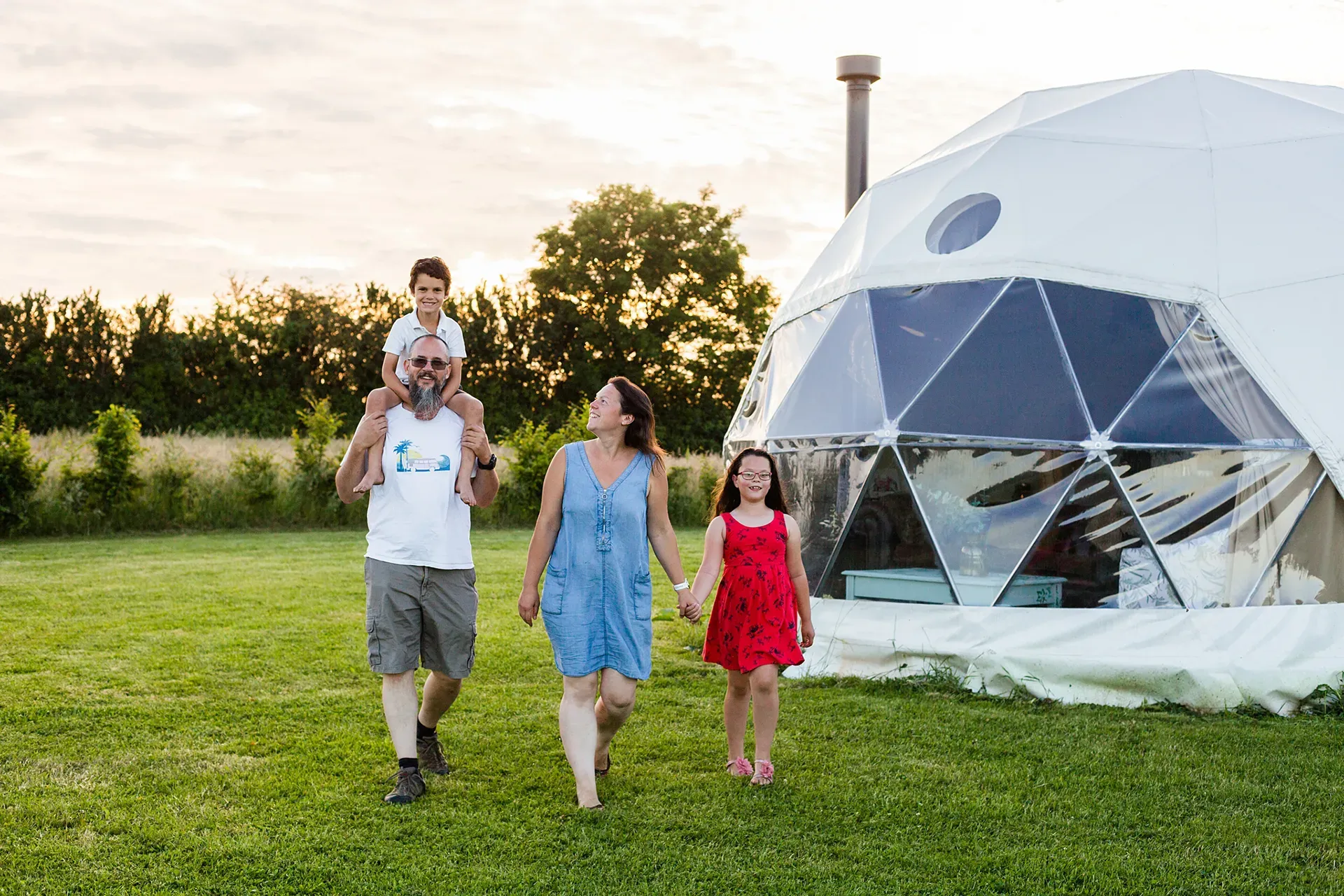 A family is walking in a field in front of a dome tent.