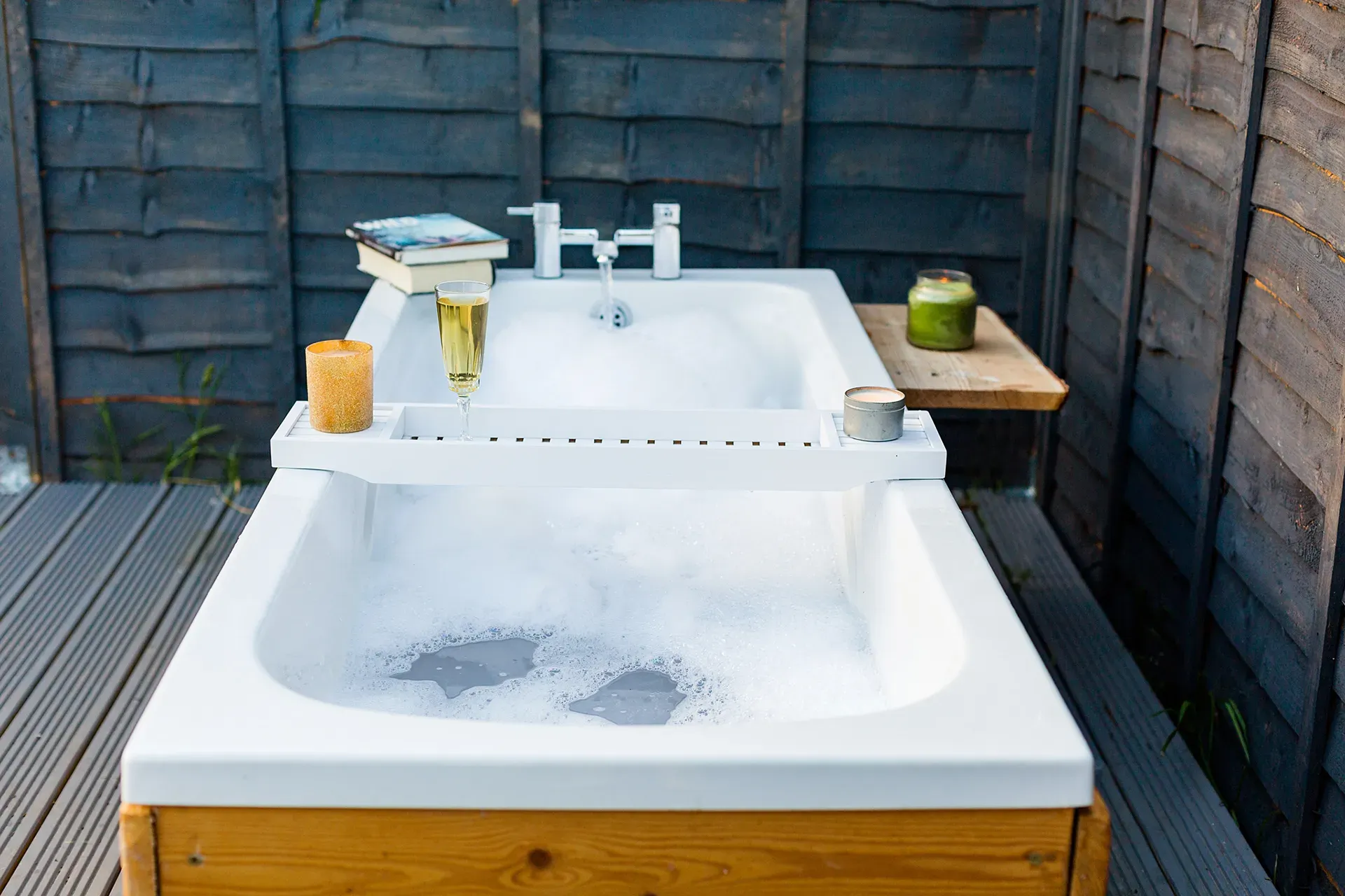 A bathtub is sitting on a wooden deck next to a wooden fence.