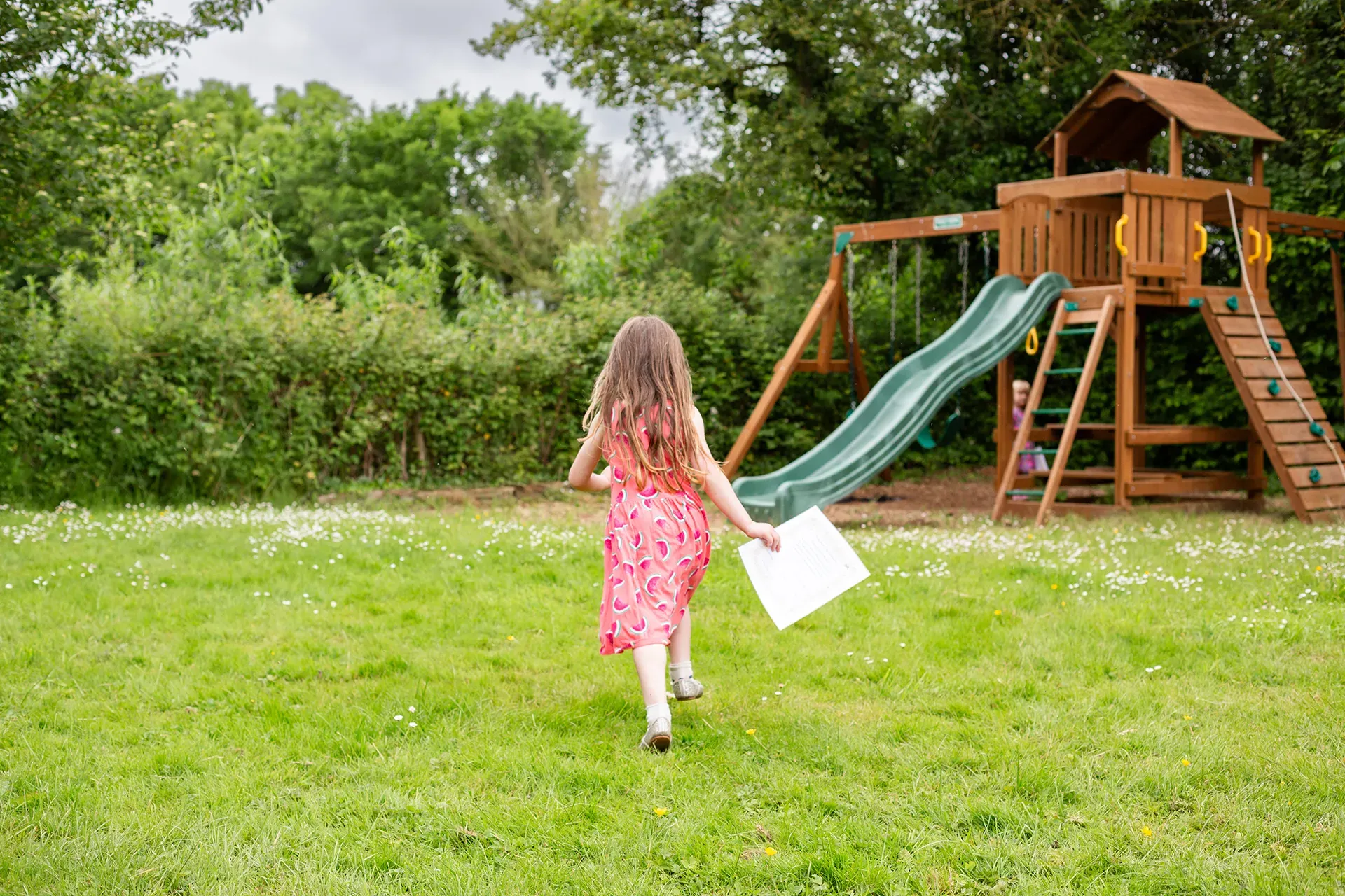 A little girl is holding a piece of paper while running in a grassy field.