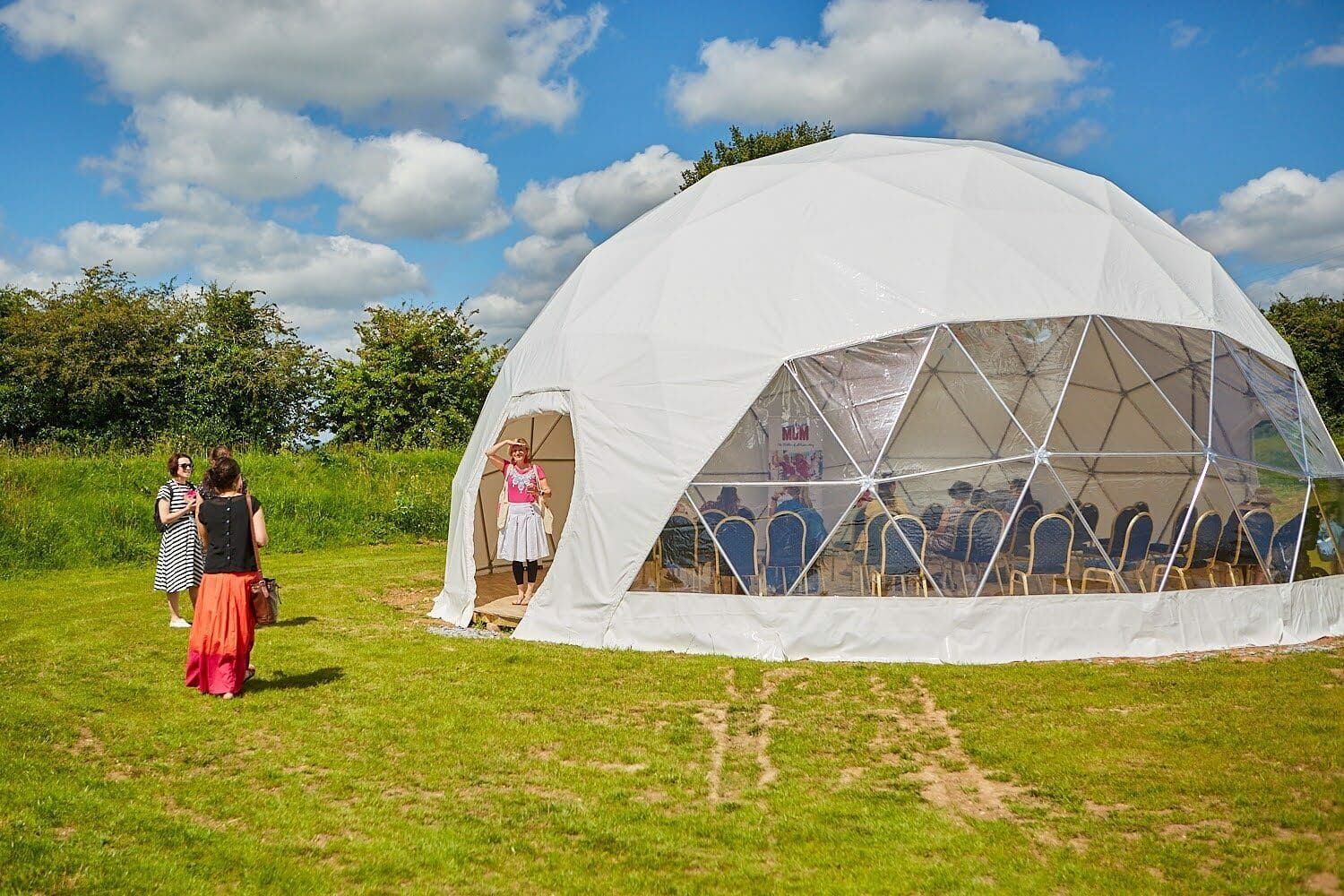 A group of people are standing in front of a dome tent in a field.