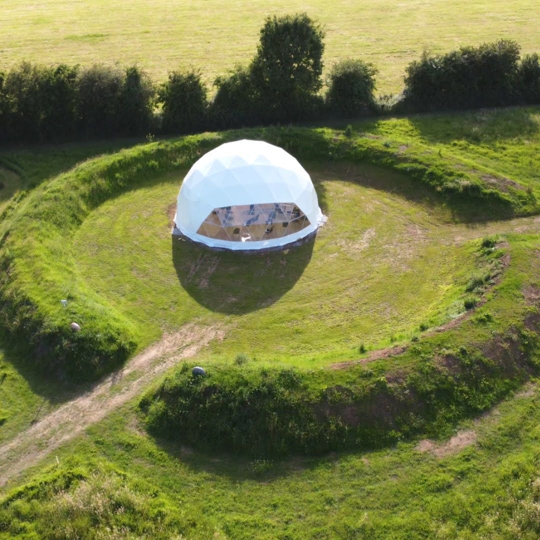 An aerial view of a dome tent in the middle of a grassy field.