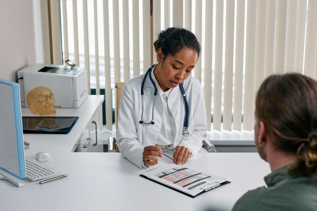 A doctor is sitting at a desk talking to a patient.