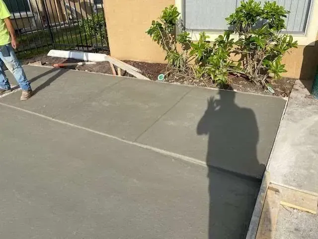 A person's shadow over fresh concrete. Construction site, new patio being built, outside.