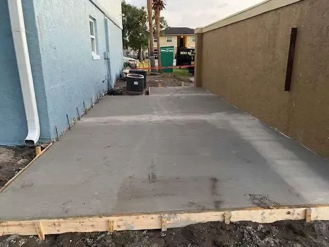 Newly poured concrete patio with wood framing, between two buildings.