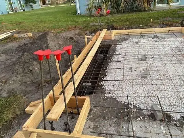 Construction site: wooden forms, rebar, gravel, and stakes set for pouring concrete.