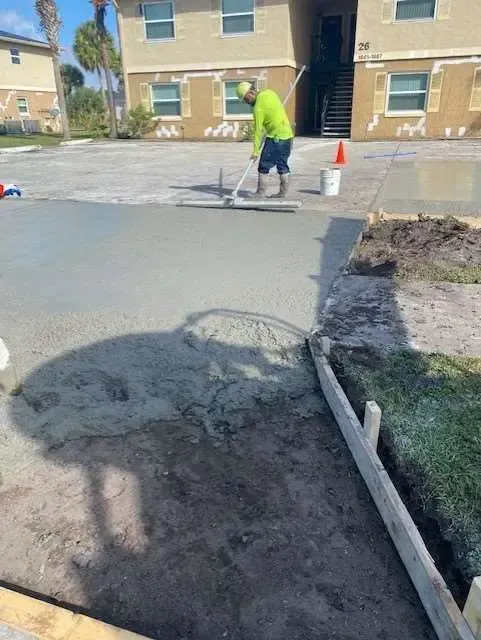 Construction worker leveling wet concrete on a walkway near an apartment building.