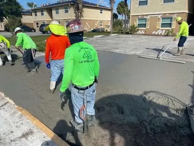 Construction workers in neon shirts paving a cement road.