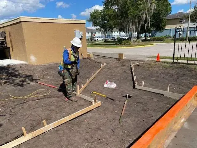 Construction worker in safety gear, setting concrete forms outdoors.