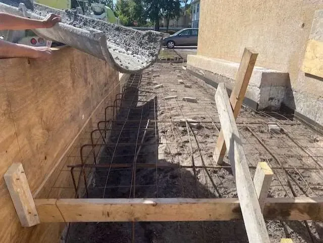 Pouring concrete into a wooden-framed foundation with rebar reinforcement; outdoor construction site.