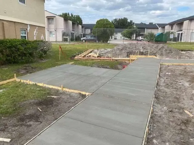 Freshly poured concrete sidewalk under construction in front of apartment buildings, sunny day.