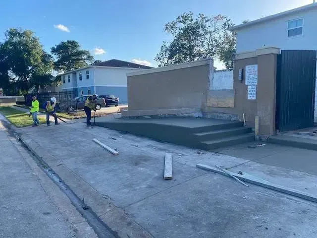 Construction workers pouring concrete ramp and steps at a building entrance.