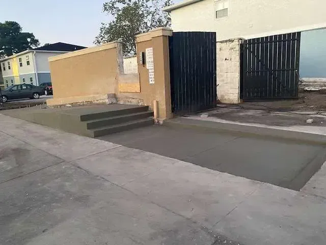 Newly poured concrete entrance with steps, gate, and tan wall next to a building.
