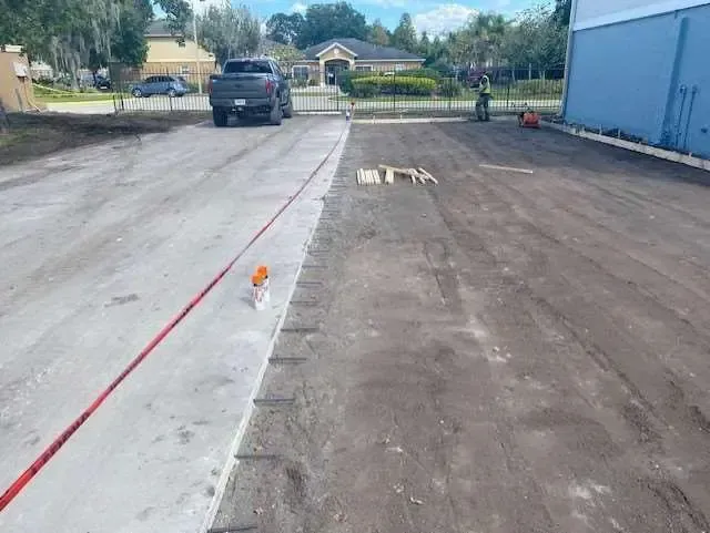 Concrete work in progress; truck and building in background; new and old pavement side-by-side.