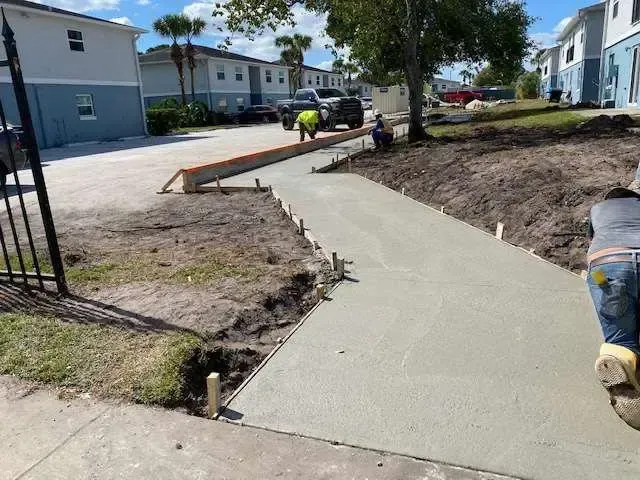 Concrete walkway under construction near buildings with workers present.