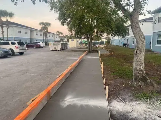 Newly poured concrete sidewalk in a residential area, next to a parking lot.