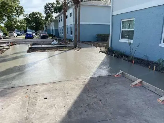 New concrete driveway and walkway construction in front of blue apartment buildings.