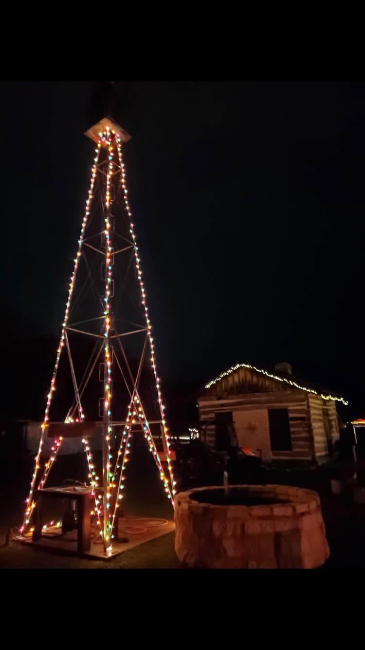 Windmill and log cabin decorated with Christmas lights at night.
