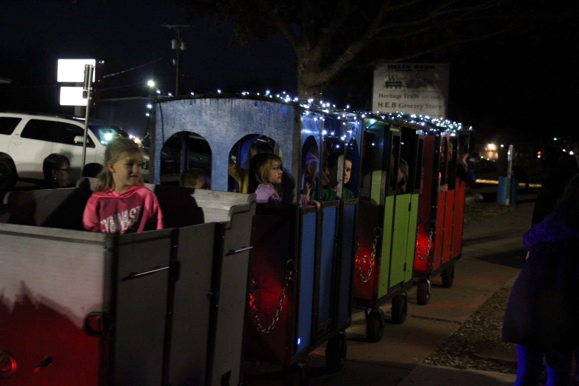 Children ride a brightly colored train decorated with lights at night.