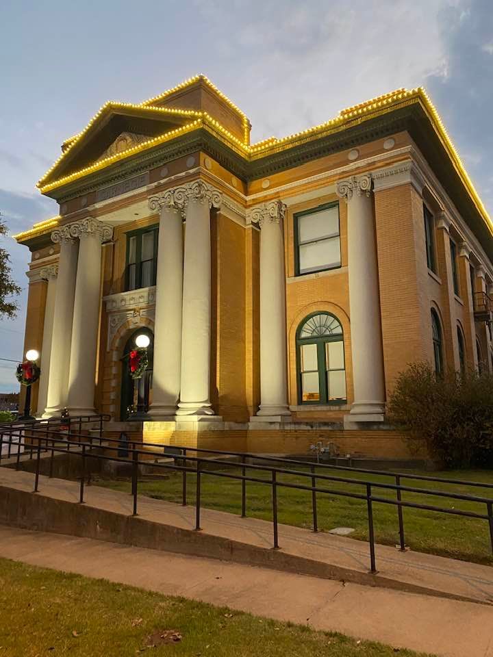Yellow brick courthouse lit with string lights. Columns frame the entrance.