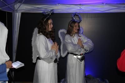 Two young women in angel costumes with wings and halos, indoors. One reads a book.