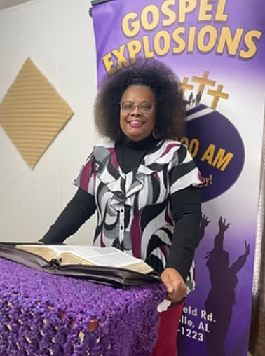 Woman at a pulpit with an open Bible, in front of a banner that reads
