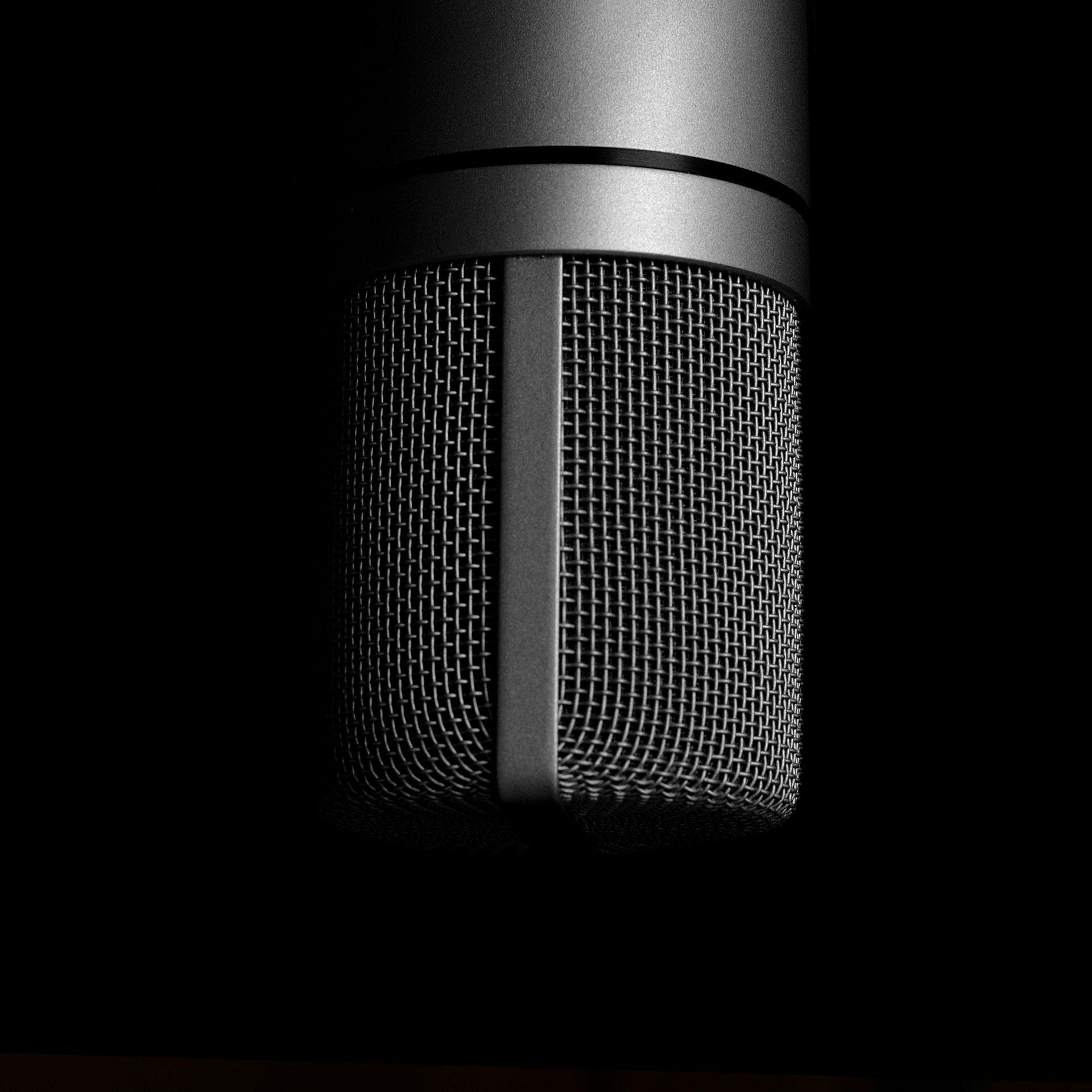 Black microphone, close-up, against dark background. The mesh grille is visible.